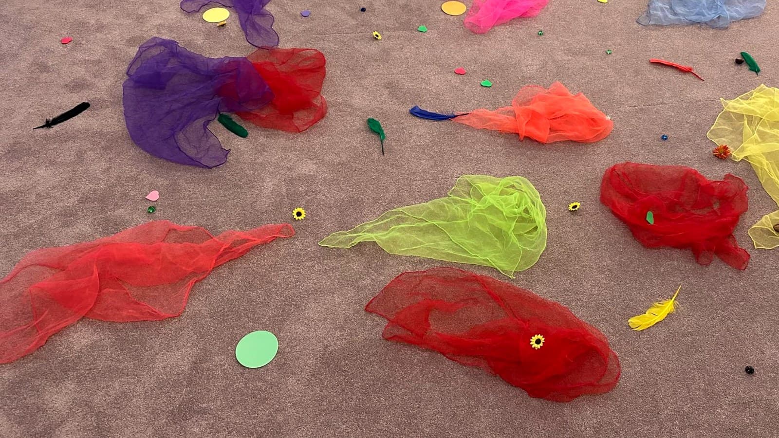 Bunte Chiffontücher, Federn und Pailletten auf dem Boden nach einer Entspannungsstunde mit Kindern